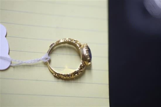 An antique yellow metal ring set with an oval sapphire in scroll-carved and pierced mount, size O.